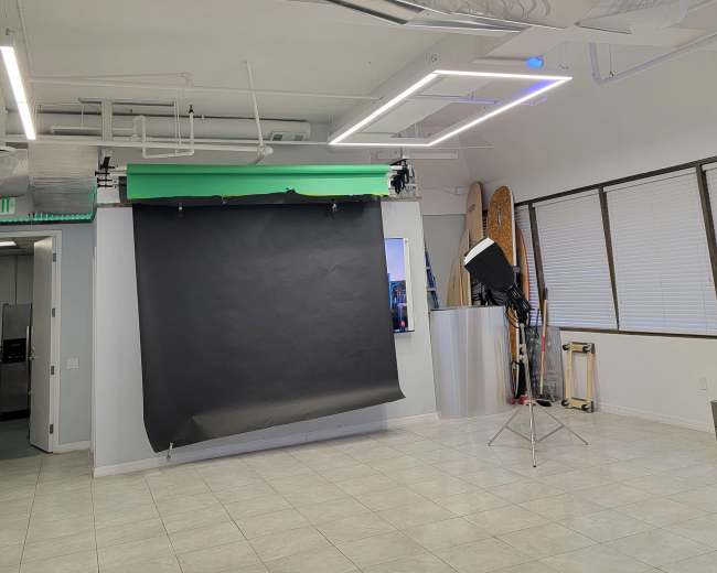 A photography studio featuring a black backdrop, a tripod with a lighting setup, and reflective silver ceiling panels.