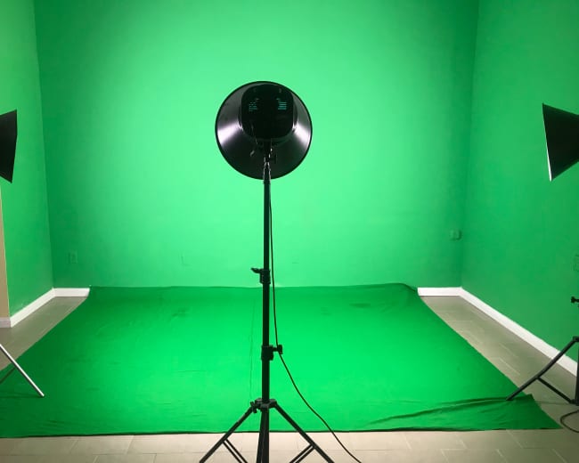 A green screen setup with a green backdrop, a round light source on a stand, and two light fixtures positioned on either side.