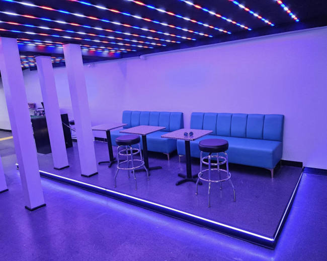 The image shows a modern lounge area with blue seating, tables, and illuminated flooring.