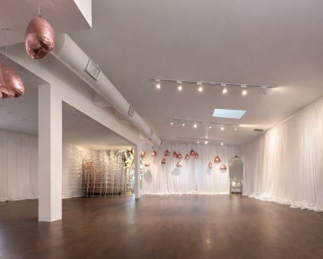 The image shows a spacious hall with a wooden floor, white drapery on the walls, and decorative elements suspended from the ceiling.