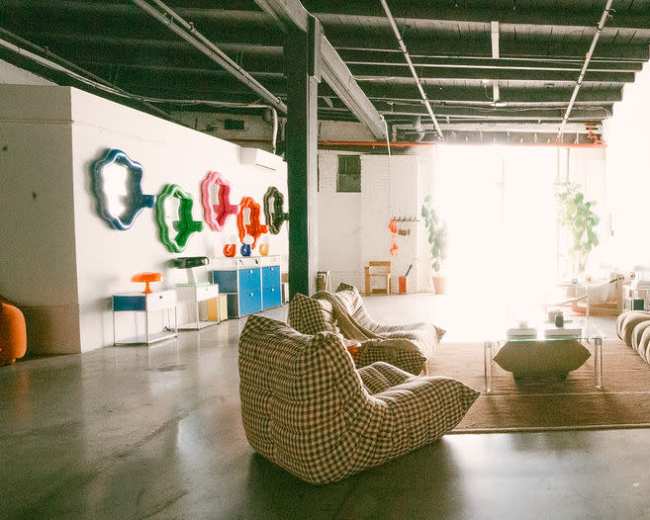 The image depicts a spacious, modern interior with various furniture pieces, including bean bags, a curved sofa, and shelves displaying decorative items.