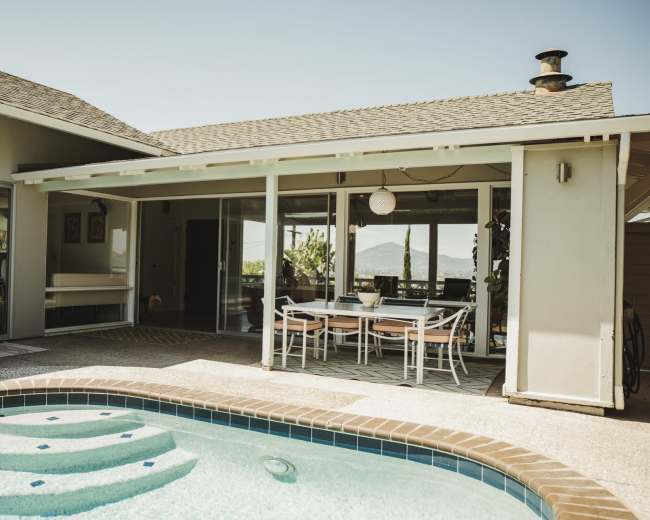 A modern home features an outdoor pool area with a seating space, large sliding glass doors, and mountain views in the background.