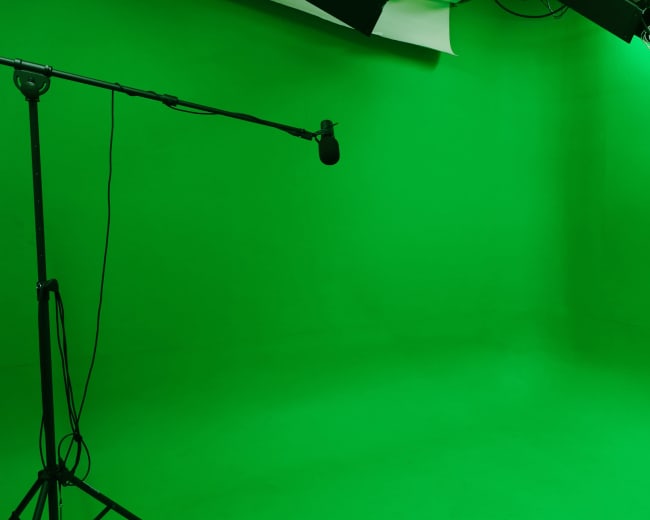 The image shows a bright green studio space with a microphone on a stand and lighting equipment overhead.