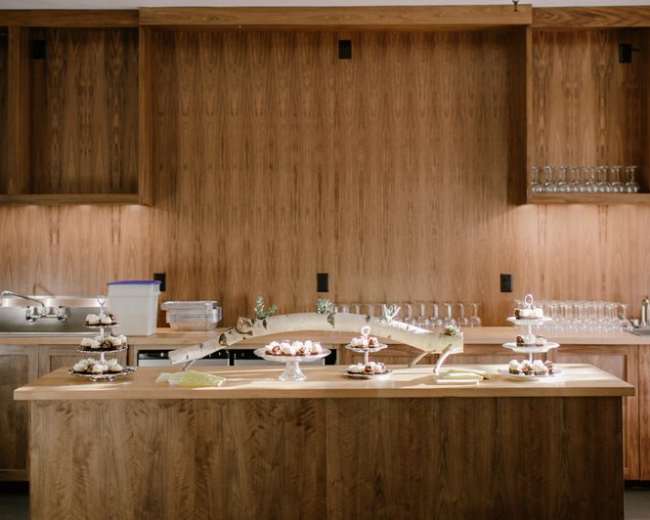 The image shows a wooden kitchen island with various desserts and a backdrop of wooden cabinetry and glassware.