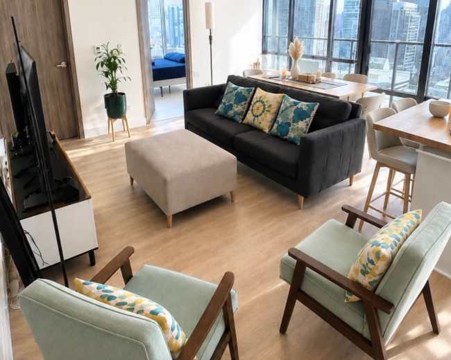 The image shows a modern living room with a gray sofa, two armchairs, a coffee table, and large windows overlooking a city skyline.