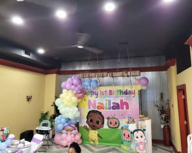 The image shows a decorated birthday party scene with a banner reading "Happy 1st Birthday Nailah" and colorful balloons.