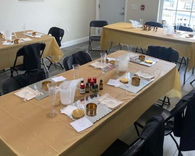 A spacious room features several tables covered with gold tablecloths, each set with materials for an activity, and black chairs arranged around them.