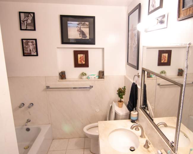 The image shows a bathroom featuring a bathtub, toilet, and a double sink vanity with framed pictures on the walls.