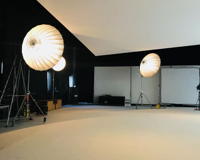 The image shows a photography studio with three large lighting setups and a blank backdrop.