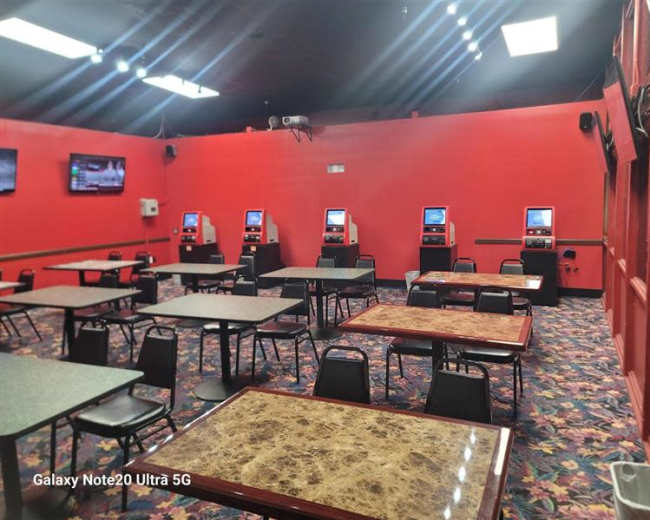 The image shows a brightly colored red room with several tables and four gaming machines lined against the wall.
