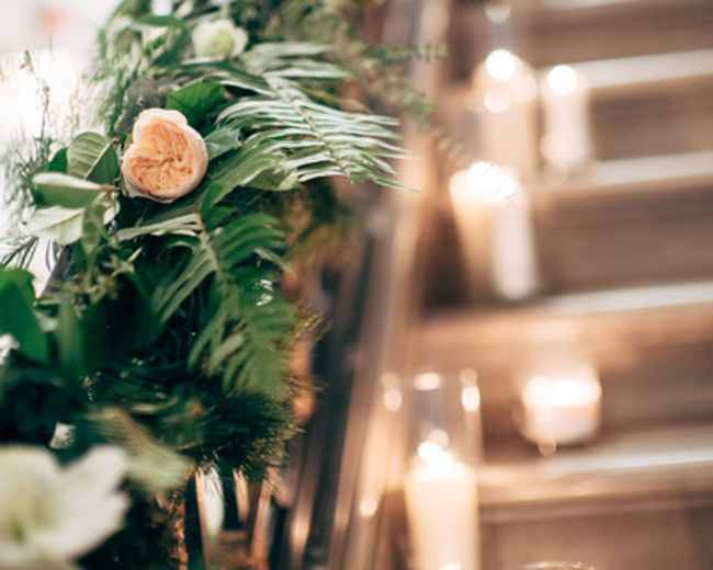 A staircase is adorned with greenery and flowers, featuring lit candles along the steps.