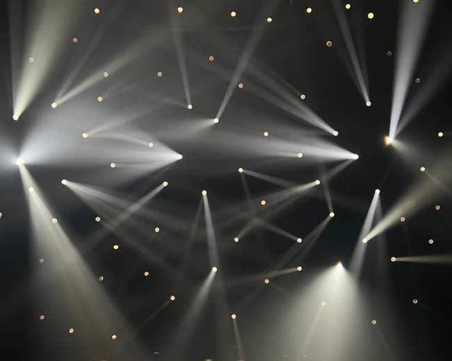 The image shows a dark scene illuminated by multiple beams of light radiating from various angles.