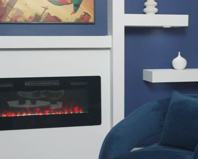 The image shows a modern living space featuring a blue accent wall, a decorative shelf with white vases, a wall-mounted electric fireplace, and a plush blue chair.