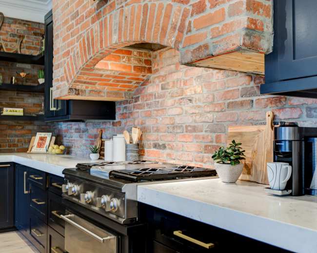 The kitchen features a brick wall backdrop, dark cabinetry, a stainless steel stove, and a countertop with modern appliances and decorative items.