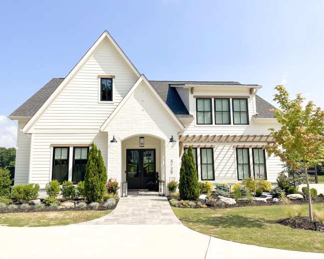 A two-story, modern-style house with white siding, black windows, and a landscaped front yard.