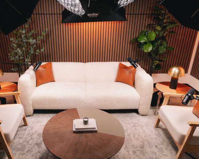 The scene shows a modern living room setup with a light-colored sofa, accent pillows, two wooden side tables, a round coffee table, and various indoor plants, all under soft lighting.
