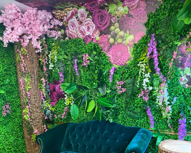 A green velvet couch positioned against a backdrop of vibrant floral decorations and lush greenery.