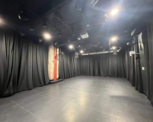 The image shows an empty stage area with black curtains, dim lighting, and a smooth floor.