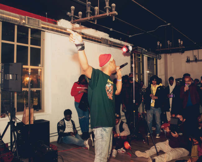 A performer on stage with a microphone captivates an audience in a crowded indoor venue.