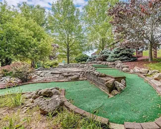 A miniature golf course featuring a winding green carpet path bordered by rocks and surrounded by trees.