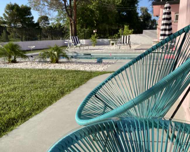 A pair of turquoise chairs are positioned beside a pool area surrounded by greenery and lounge chairs.