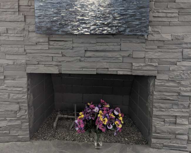 A large painting of a mountainous landscape is hung above a stone fireplace, with a vase of flowers in front.