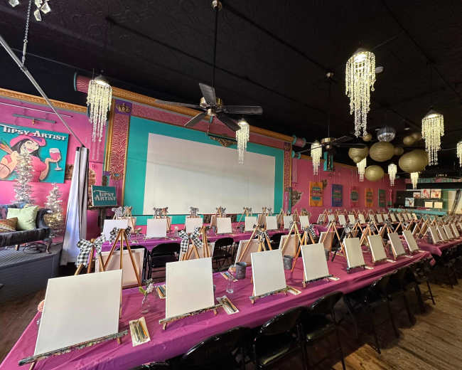 A brightly colored art studio set up with multiple easels and blank canvases arranged around a long table.