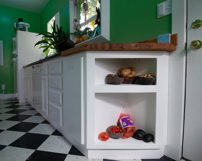 A kitchen with green walls, a checkered floor, and a white countertop featuring a shelf with various fruits and vegetables.