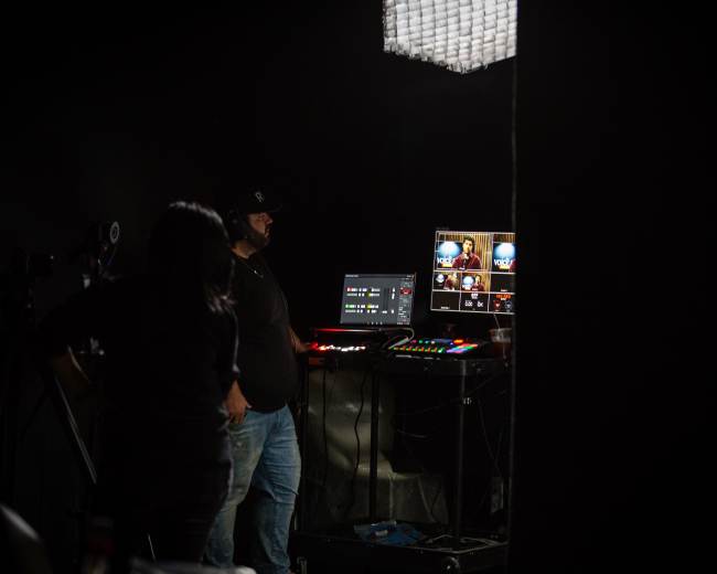 A person operates a video production setup in a dimly lit room.