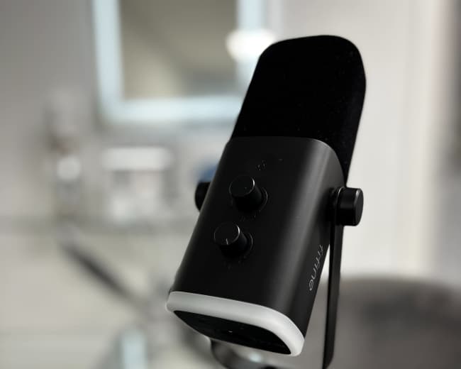 The image shows a black microphone on a circular stand placed on a glass table.