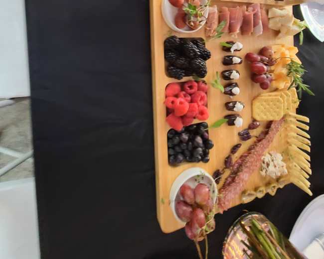A wooden charcuterie board arranged with various cheeses, meats, fruits, nuts, and crackers, alongside a circular platter of assorted snacks.