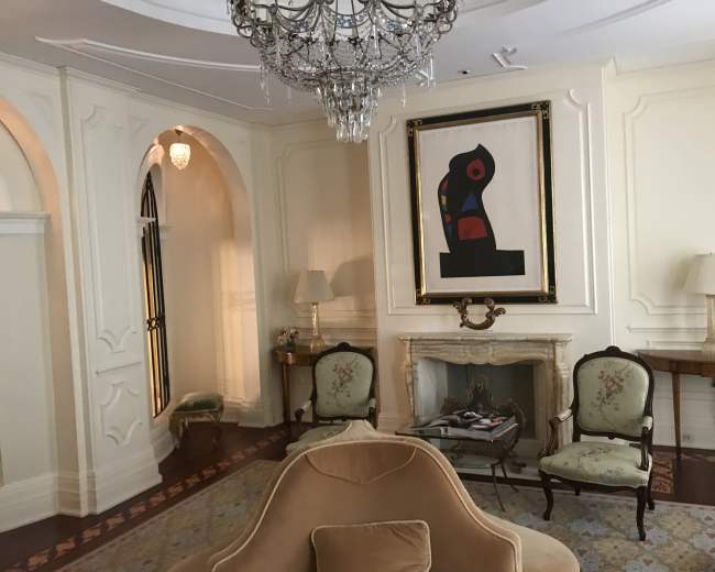 An elegantly designed room featuring a chandelier, a framed artwork, and two floral-patterned armchairs arranged near a fireplace.