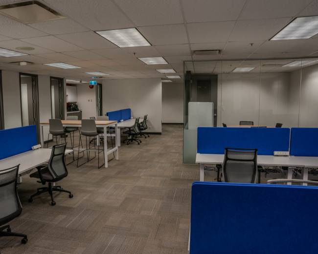 The image shows an open office space featuring several workstations with blue dividers, desks, and chairs arranged in a grid layout.