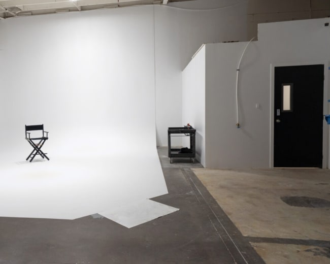 A single director's chair is positioned on a vast, empty white backdrop within a studio space.