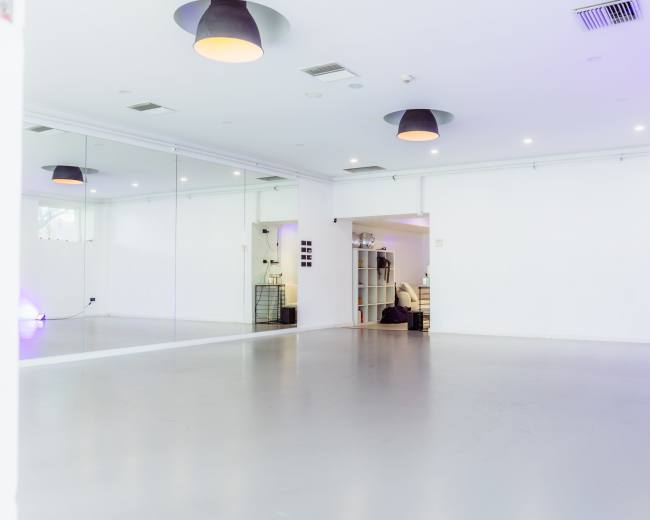 The image shows a spacious, empty dance studio with mirrors on one wall and soft lighting.