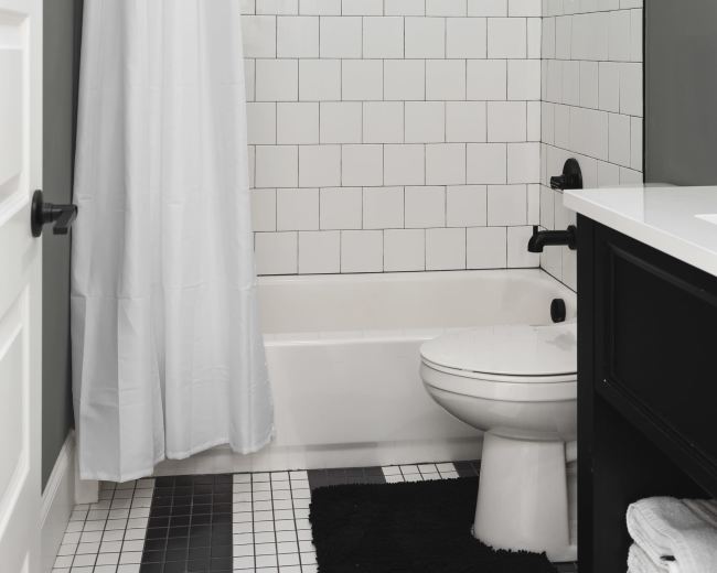 The image shows a modern bathroom featuring a bathtub with a shower curtain, white tiled walls, and black accents.