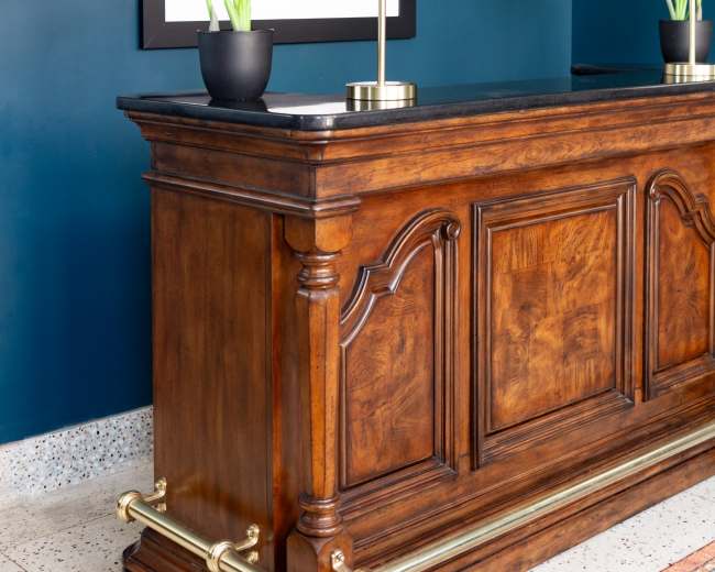 A wooden sideboard with decorative features stands against a blue wall, flanked by potted plants and illuminated by lamps.