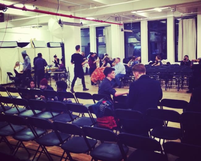 A spacious room with rows of empty chairs, where people are preparing for an event, while others are seated and interacting.