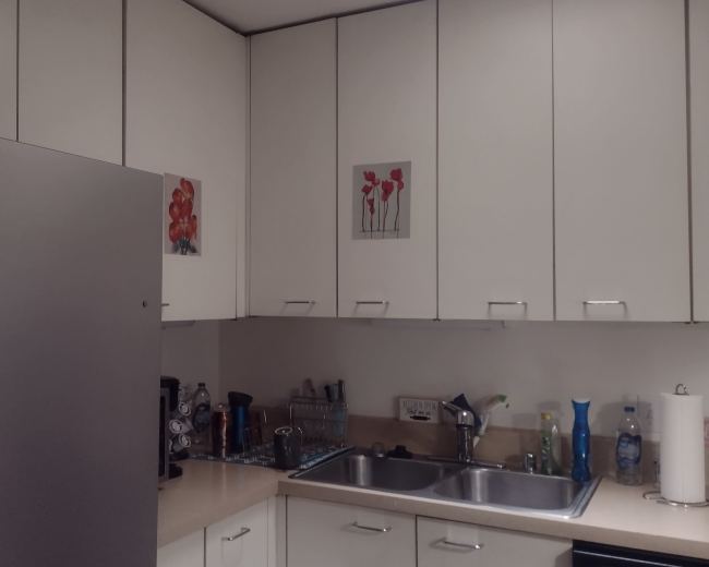 The image shows a modern kitchen with white cabinets, a stainless steel refrigerator, a sink, and various kitchenware on the counter.