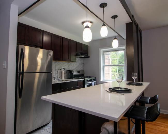 A modern kitchen features dark wood cabinets, stainless steel appliances, and a white countertop with bar seating.