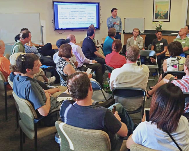 A group of people is seated in a circle attending a presentation in a conference room.