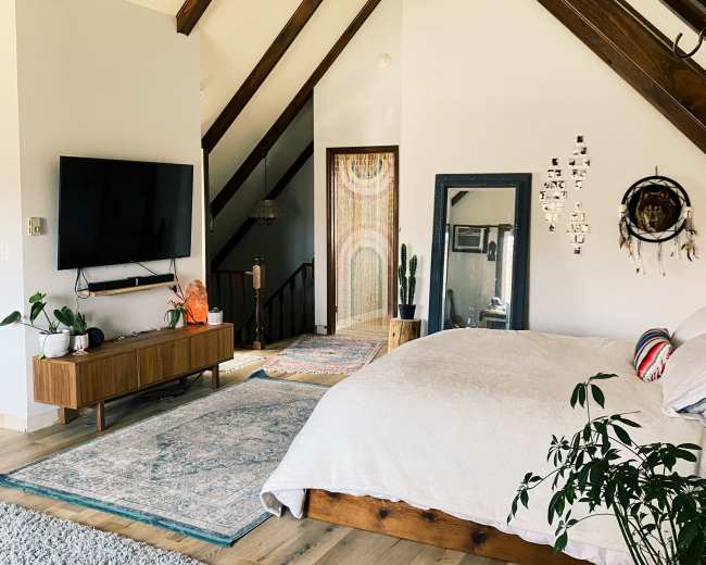 A spacious bedroom features a wooden bed, a large TV mounted on the wall, and a staircase leading to an upper level.