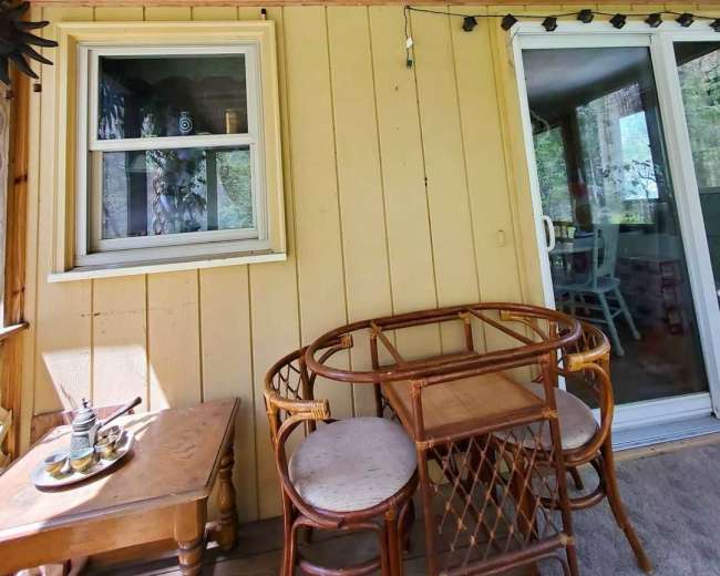 The image shows a small outdoor seating area with a round table and two chairs, adjacent to a yellow wooden wall and a sliding glass door.