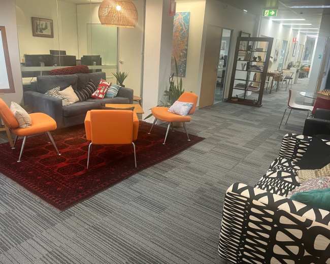 The image shows a modern office interior with colorful seating areas, a patterned sofa, and various decorative elements in a well-lit space.