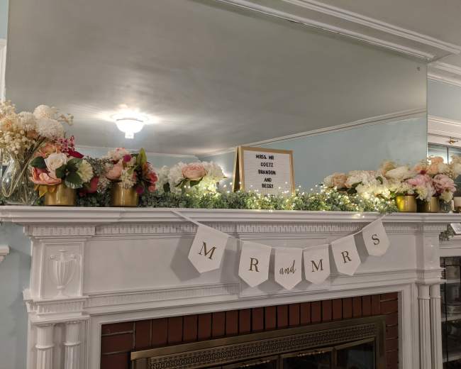 A decorated mantel features a floral arrangement, a sign, and a banner that reads "MR and MRS."