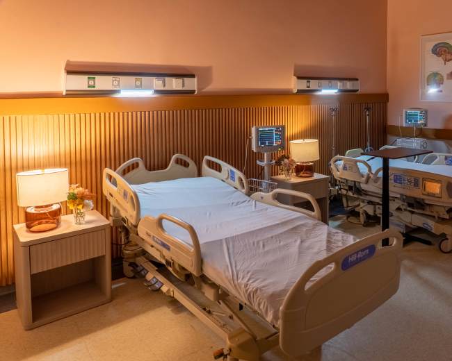 The image shows a hospital room with three adjustable beds, bedside tables with lamps, and medical monitors on the walls.