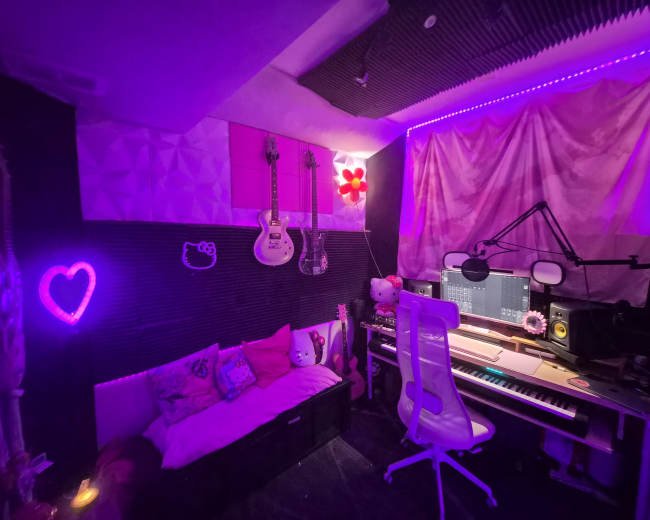 The image shows a music studio decorated with vibrant purple lighting, featuring musical instruments on the wall, a keyboard, and a cozy seating area.