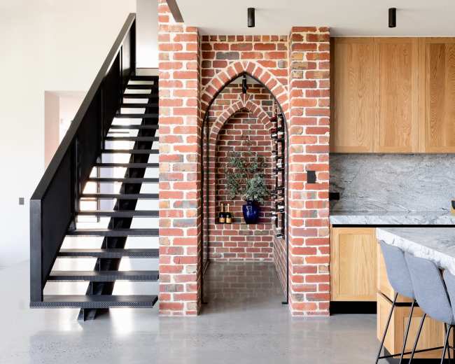 A modern kitchen with a brick archway and a staircase leading to an upper level.