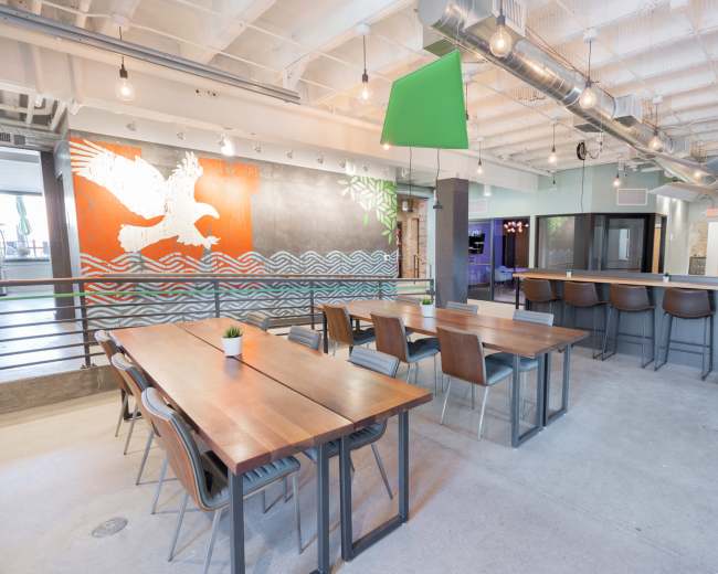 A modern office space features a large mural of an eagle, wooden tables, and a sleek bar area under bright overhead lights.