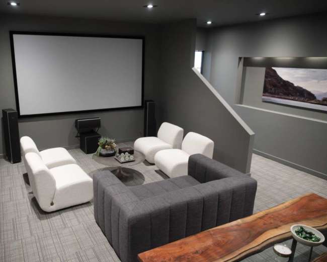 The image shows a modern home theater with a large screen, comfortable seating arranged in a U-shape, and minimalist decor.